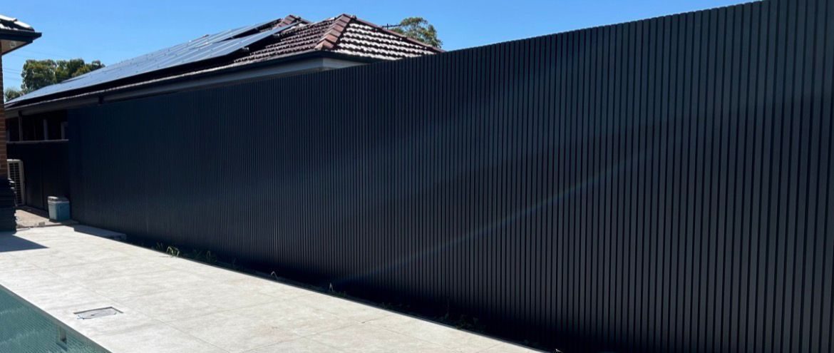 Fencly WPC Cladding: black fluted composite wall cladding running the length of a poolside courtyard.