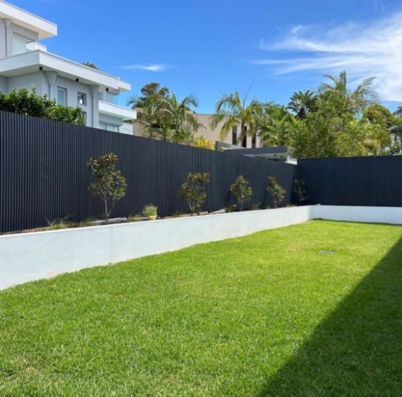 Fencly WPC Cladding: charcoal fluted composite boards cladding a low boundary wall with garden planting.