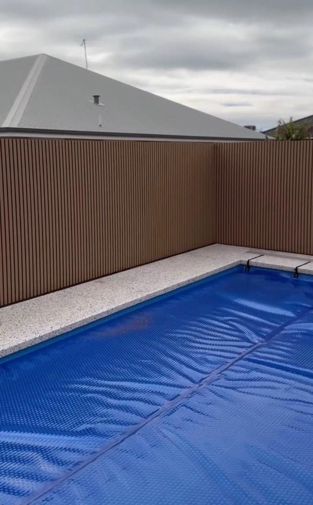 Fencly WPC Cladding: teak fluted composite cladding wrapping a swimming-pool surround.